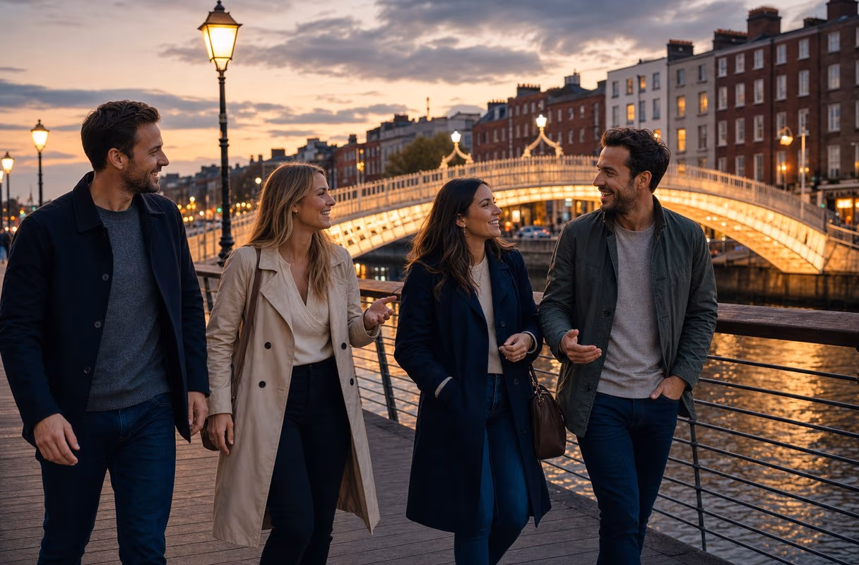 Four people walking along the Liffey boardwalk in Dublin at dusk, the Ha'penny Bridge lit behind